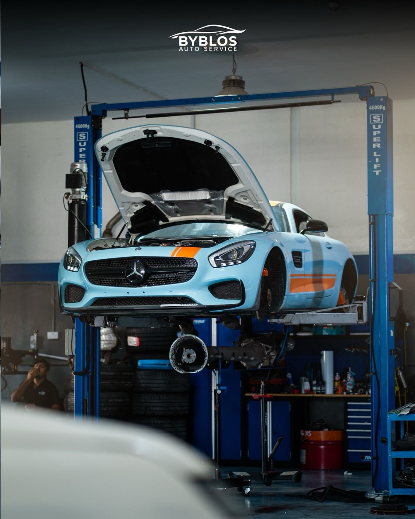 A light blue and orange Mercedes-AMG GT raised on a blue two-post lift