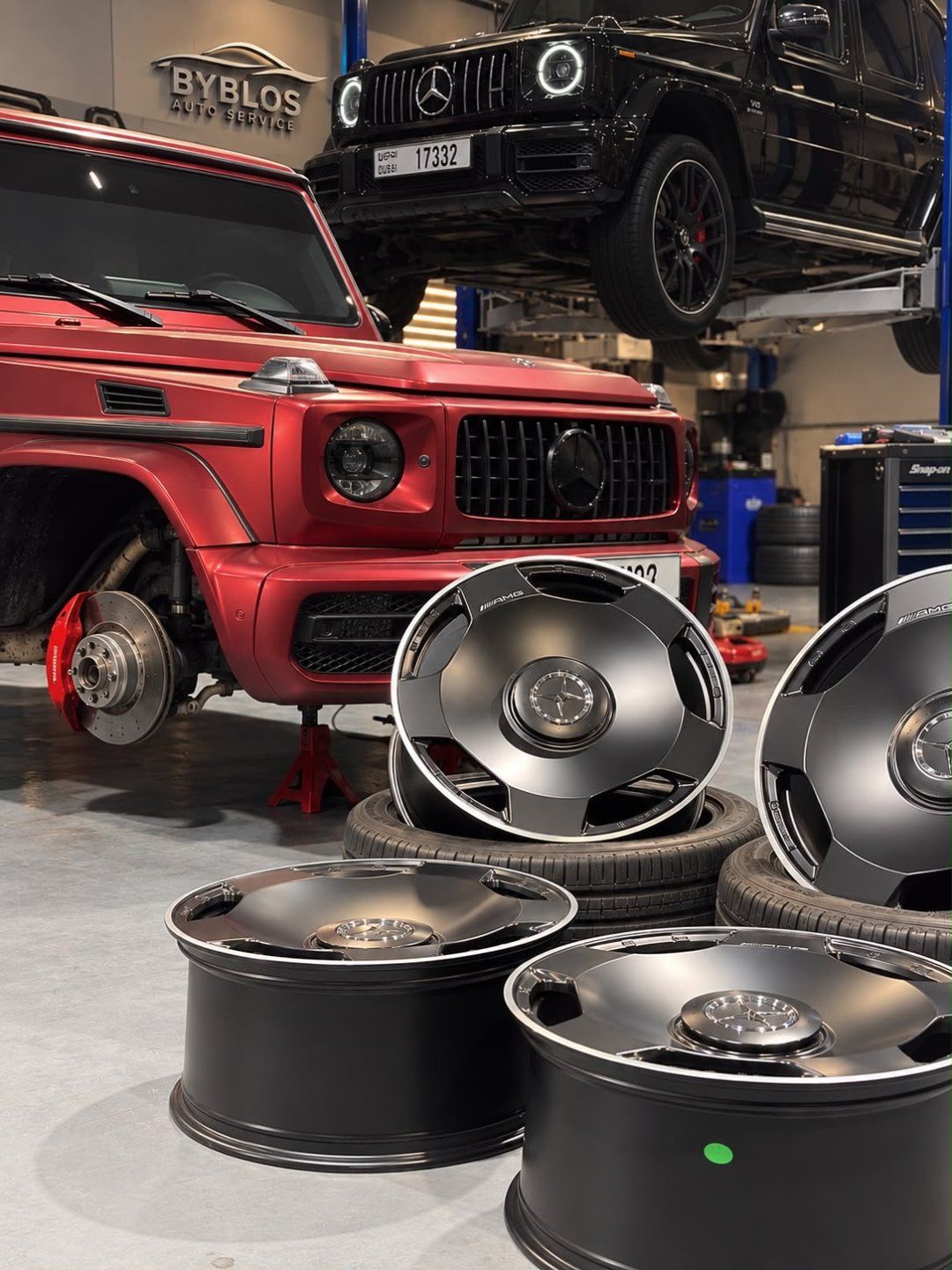 A red Mercedes G 63 raised on stands with new black wheels laid out in front of it