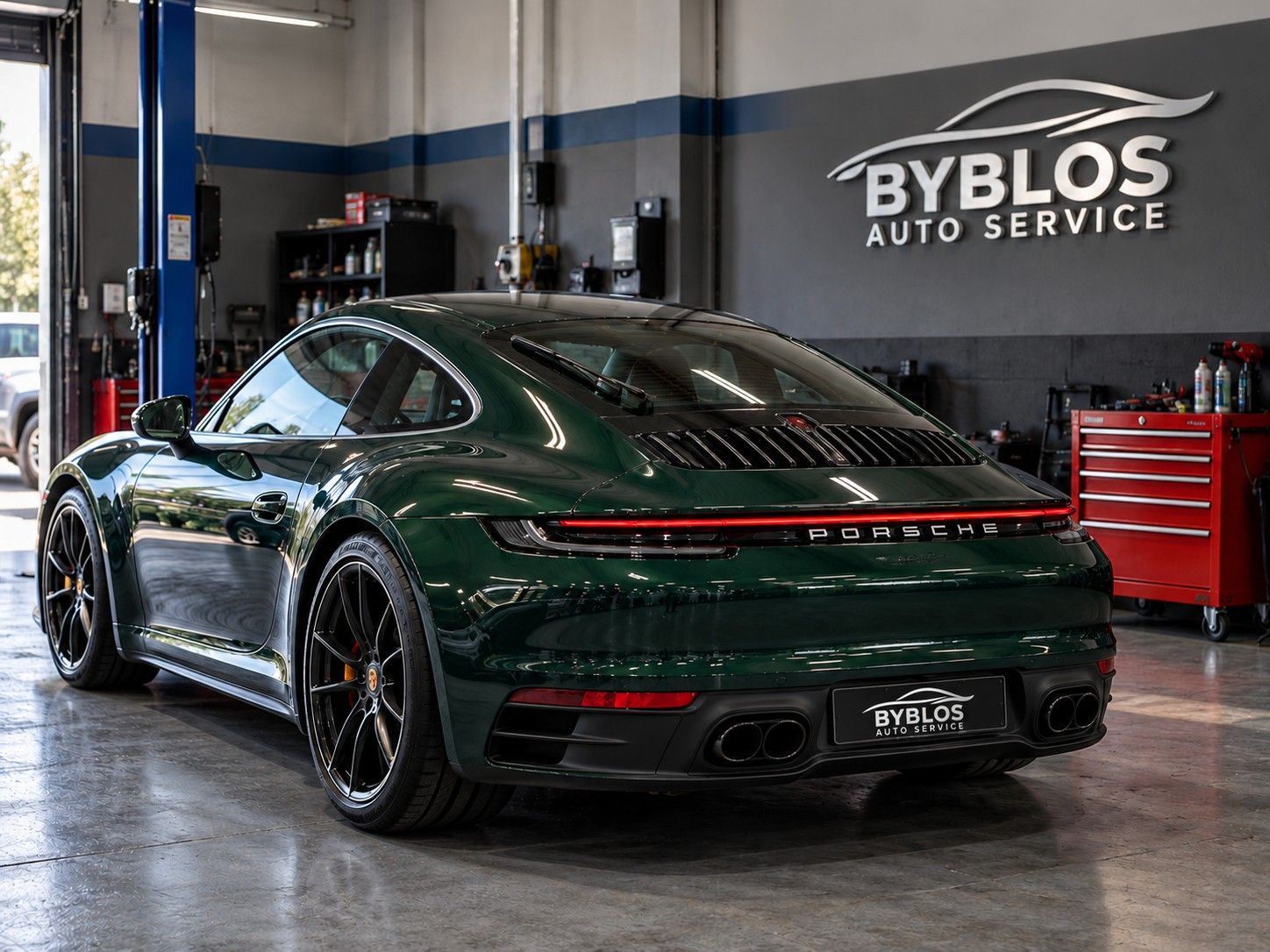 A green Porsche 911 from the rear, its full-width light bar lit, in the BYBLOS workshop